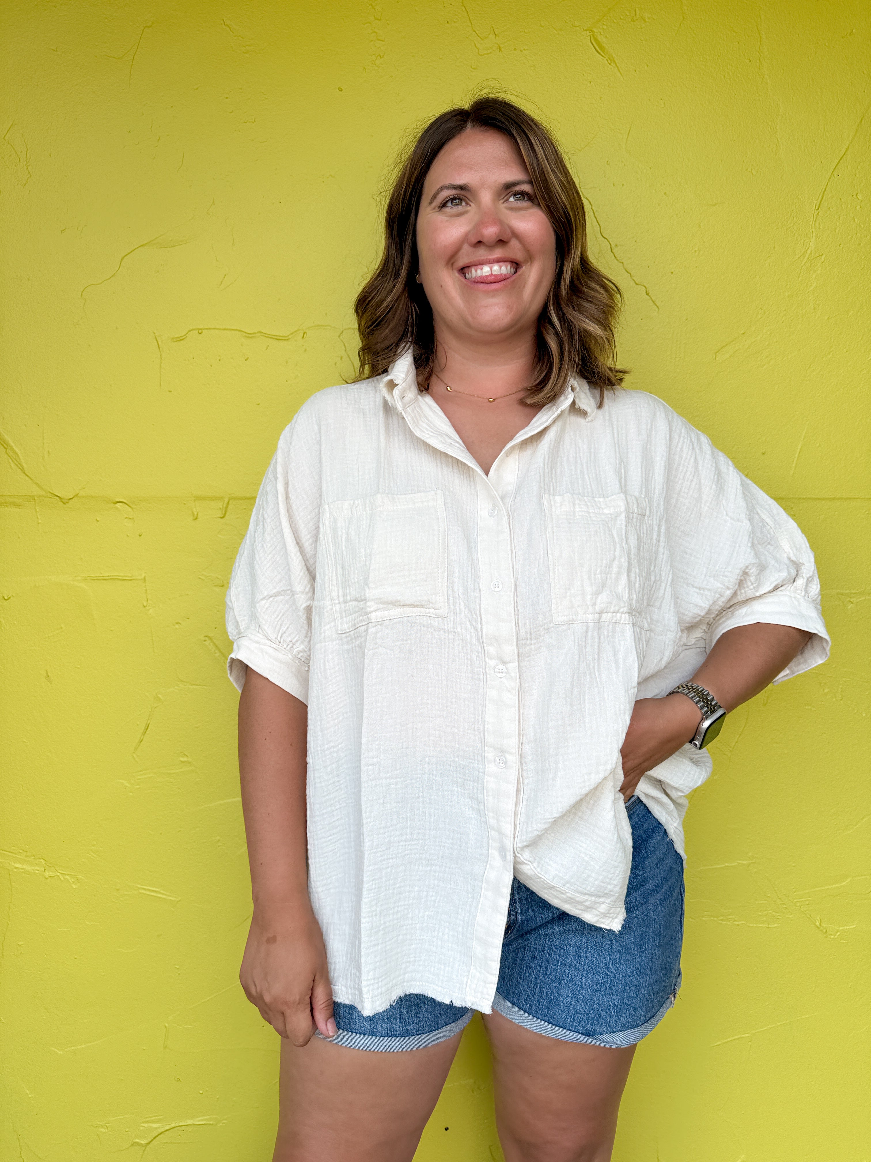 Woman wearing a white shirt and denim shorts against a yellow wall