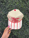 Beige cap with red text and white pattern held against a green textured background