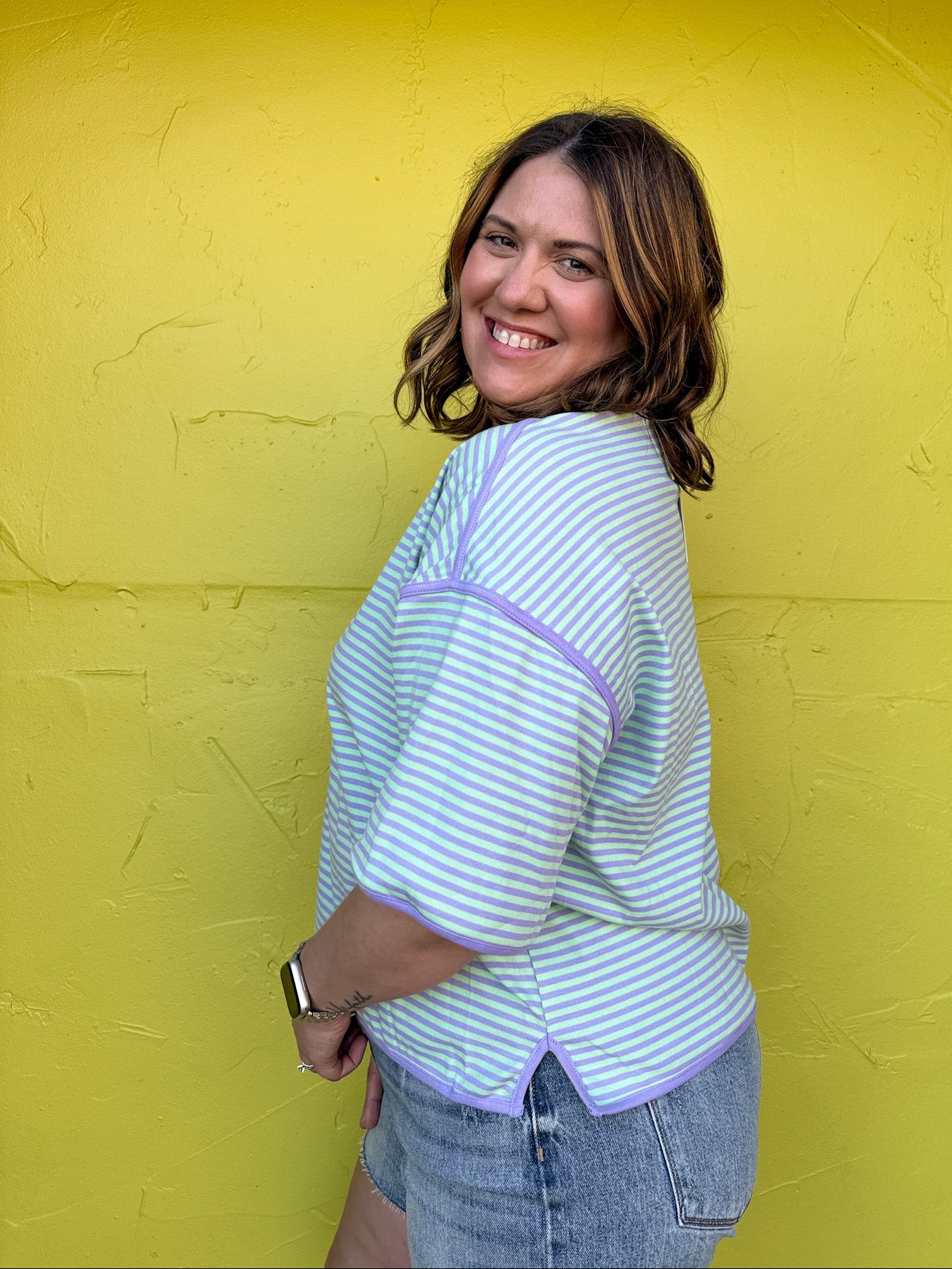 Woman wearing a light blue striped shirt against a yellow wall